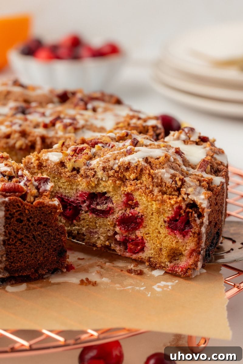 A beautiful slice of cranberry coffee cake being carefully lifted away from the remaining cake on a white cake server.