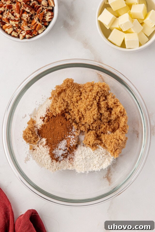 Overhead view of flour, brown sugar, cinnamon, and salt measured into a clear glass mixing bowl, ready for the streusel topping.