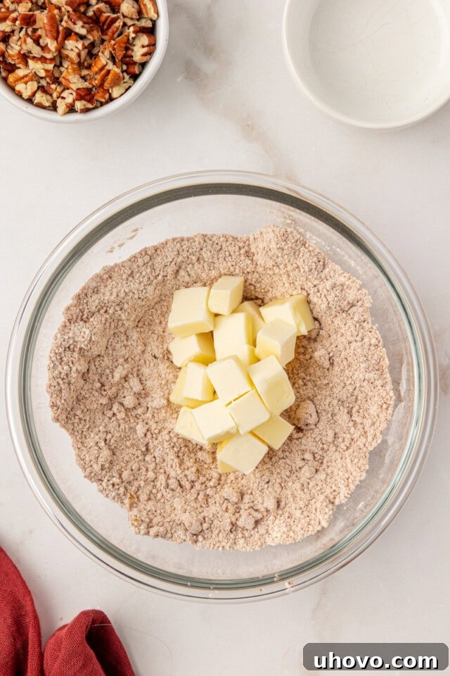 Overhead view of cold, cubed butter being added to the streusel dry mixture in a glass bowl, ready to be cut in.