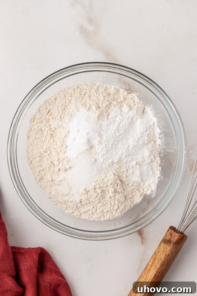 Overhead view of all-purpose flour, baking powder, baking soda, and salt measured into a glass mixing bowl, combined for the cake batter.