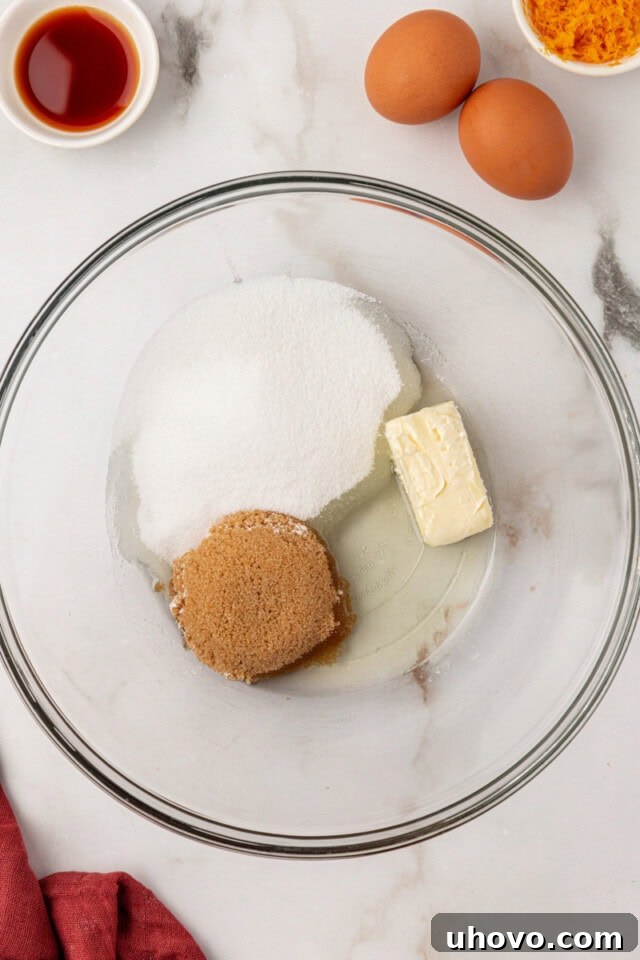 Overhead view of softened butter, neutral oil, granulated sugar, and brown sugar being creamed together in a glass mixing bowl for the cake batter.