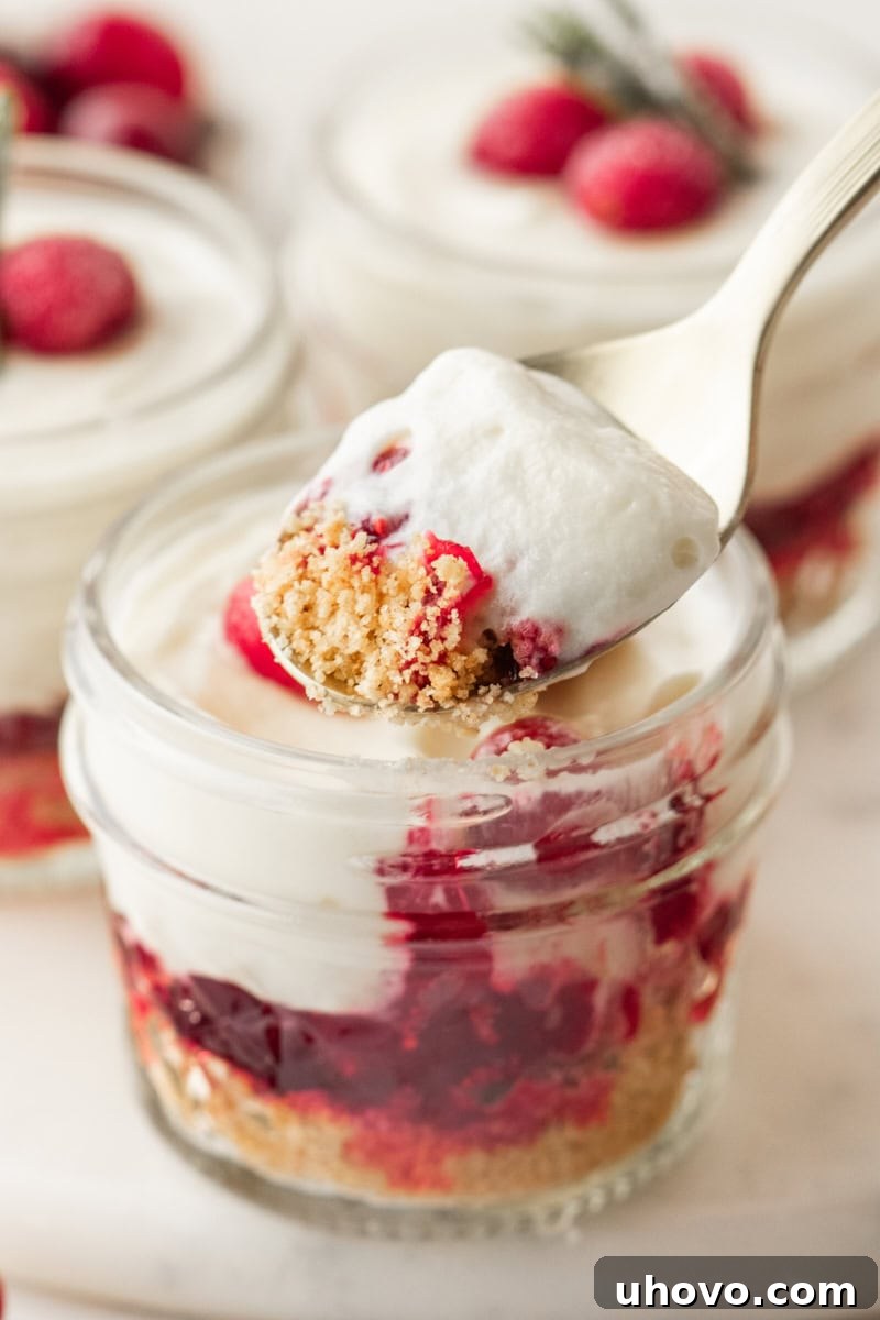 a spoonful of no-bake white chocolate cranberry cheesecake on a spoon with cranberry cheesecake jars in the background