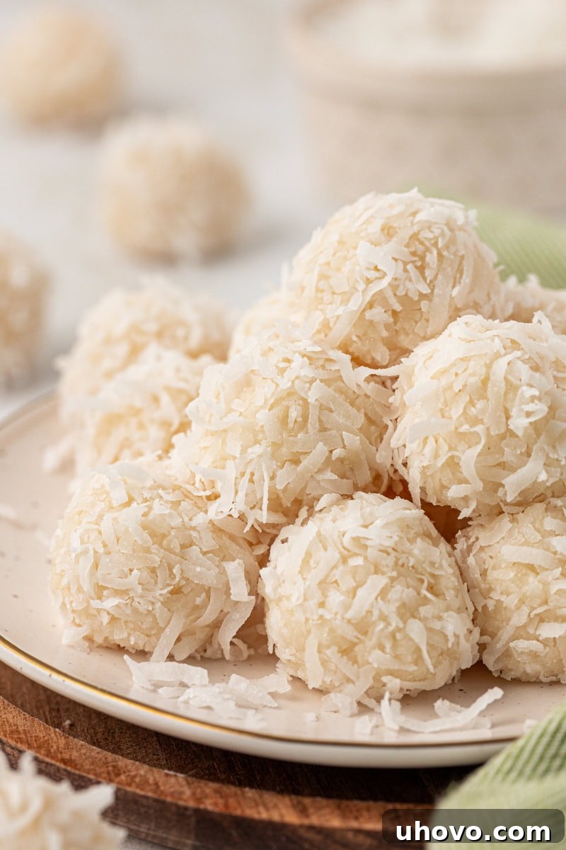 several coconut snowballs piled on a white plate with more snowballs in the background