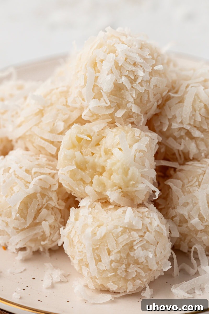 a pile of coconut snowballs on a white plate with a bite missing from one of them