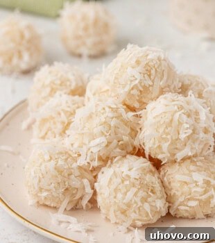 coconut snowballs served on a white plate with more of the candies in the background