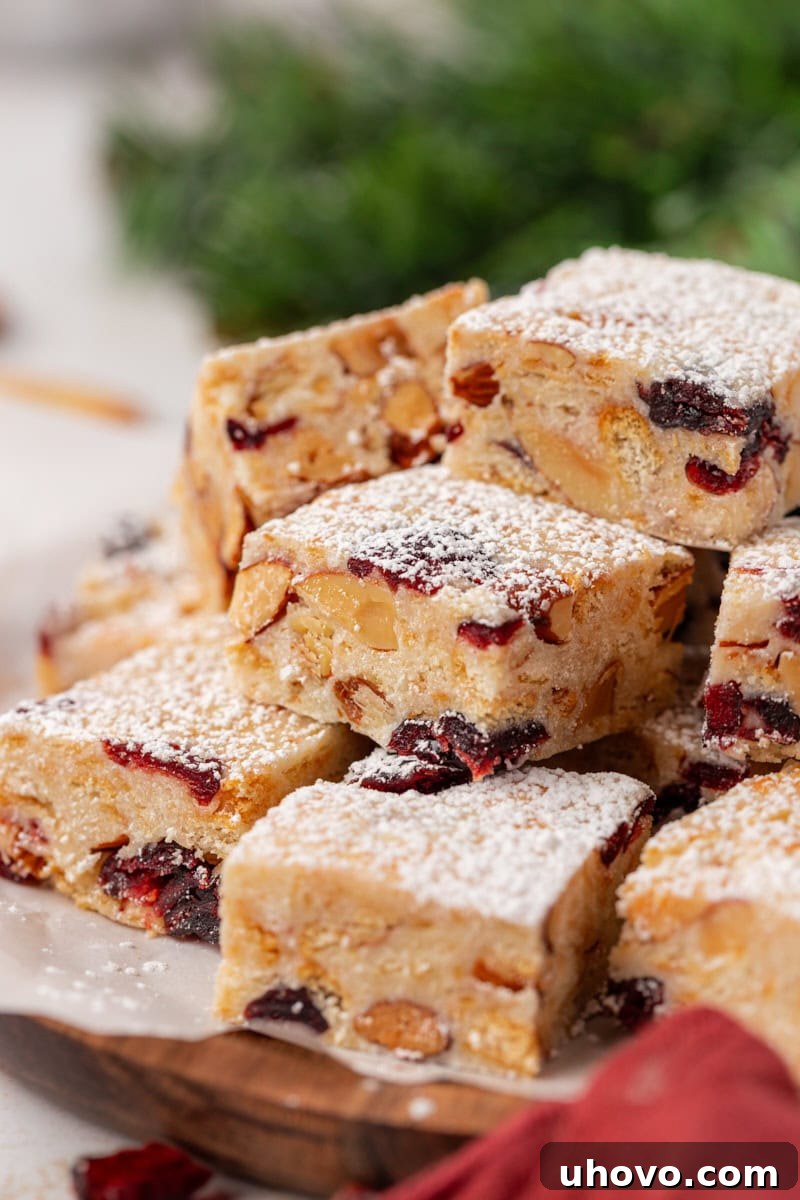 Snowflake Crisp bars, a no-bake holiday treat, artfully arranged on parchment paper. The bars feature white chocolate, marshmallows, buttery crackers, dried cranberries, and nuts, all dusted with powdered sugar for a festive look.