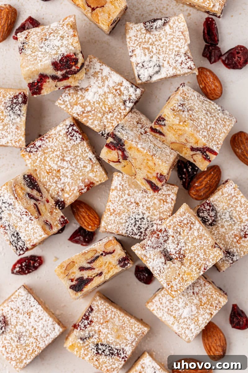 Overhead view of Snowflake Crisp pieces scattered on parchment paper, accompanied by loose almonds and dried cranberries, illustrating the delicious ingredients.