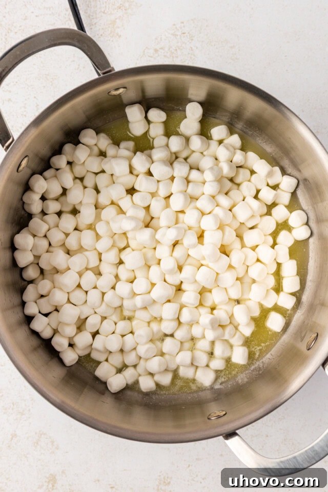 Overhead view of mini marshmallows added to melted butter in a large saucepan, preparing the base for Snowflake Crisp.