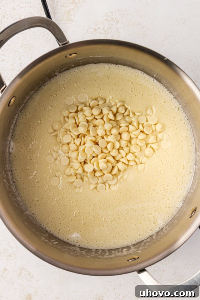 Overhead view of white chocolate chips being added to the warm butter and marshmallow mixture in a saucepan, ready to be melted and incorporated.