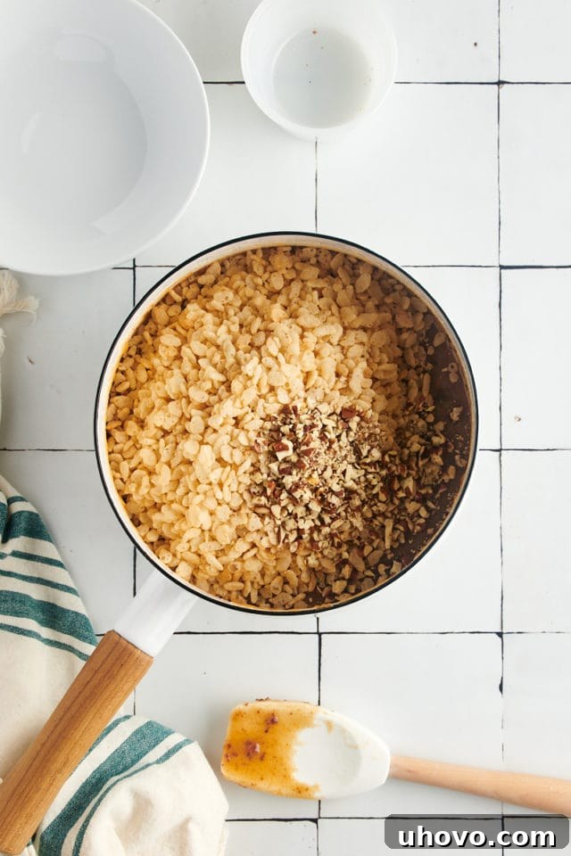 Overhead view of crisp rice cereal and chopped pecans being folded into the cooled date mixture in a pan