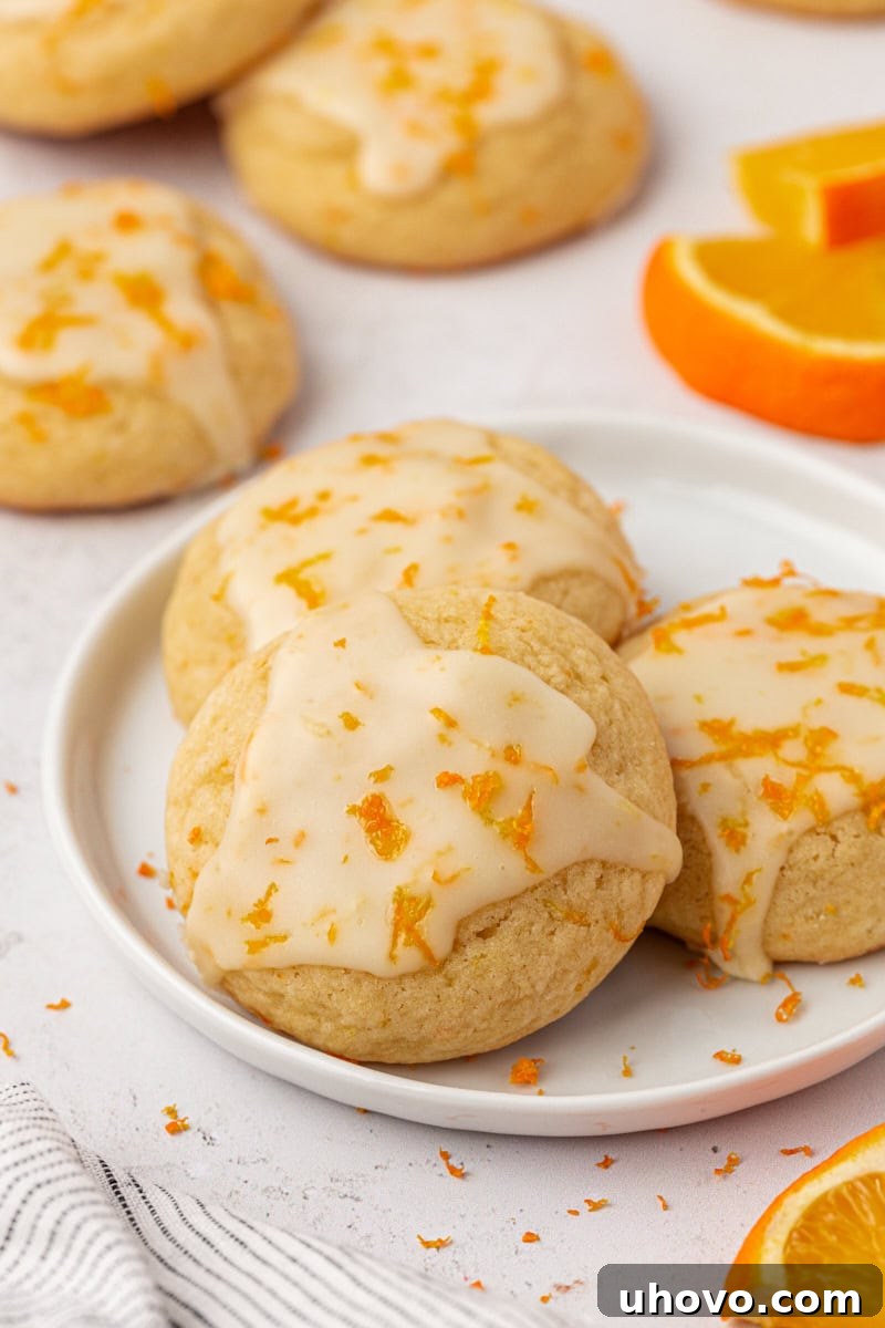 three glazed orange cookies on a white plate with more cookies in the background