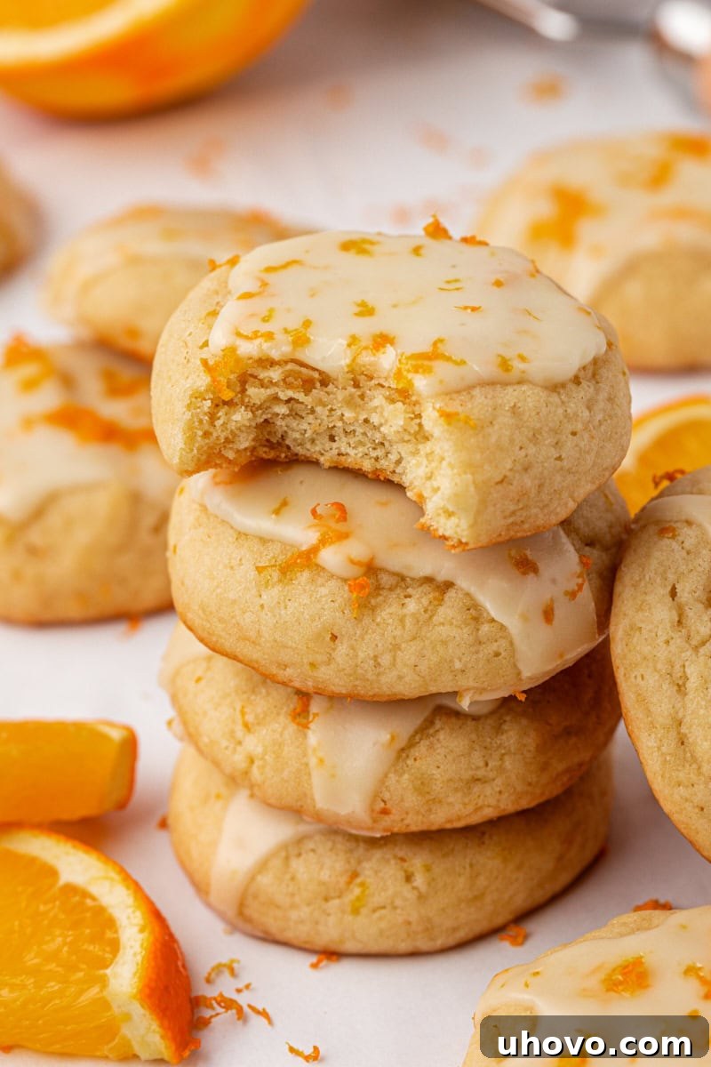 a stack of four glazed orange cookies with a bite missing from the top cookie