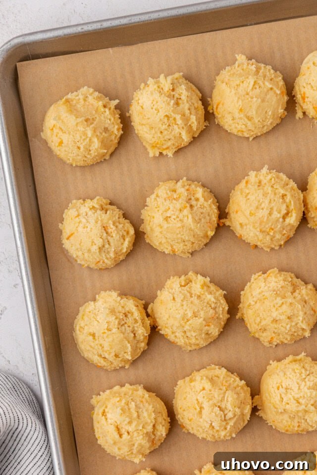 overhead view of scooped orange cookie dough on a parchment-lined baking sheet
