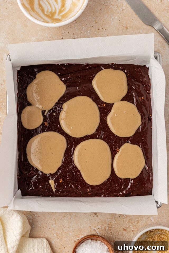 overhead view of tahini dolloped over brownie batter in a square baking pan