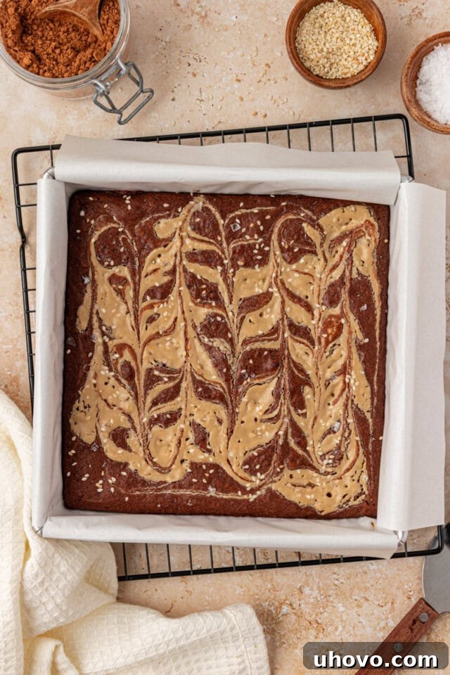 overhead view of freshly baked tahini brownies in a square baking pan cooling on a wire rack