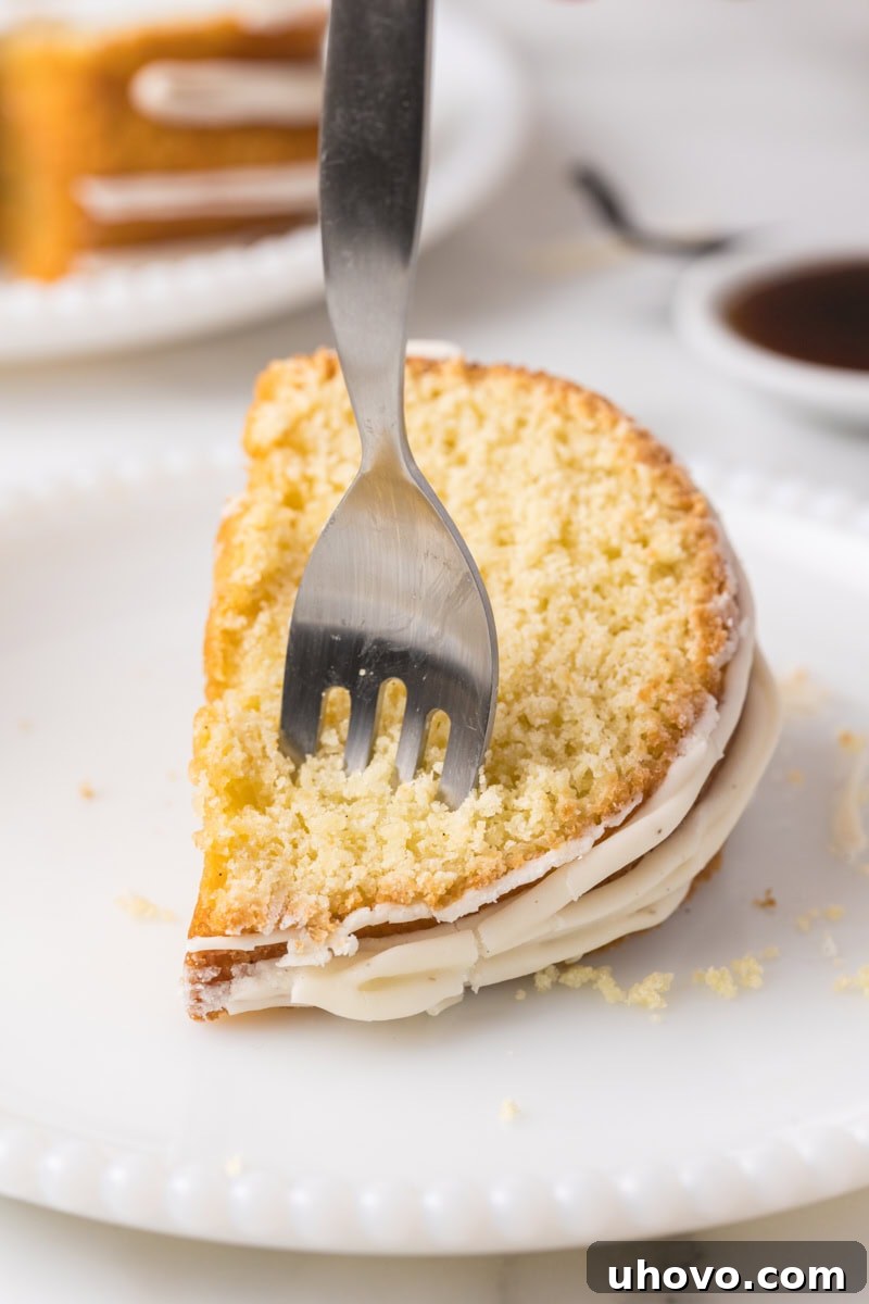 a fork cutting into a slice of vanilla Bundt cake on a white plate