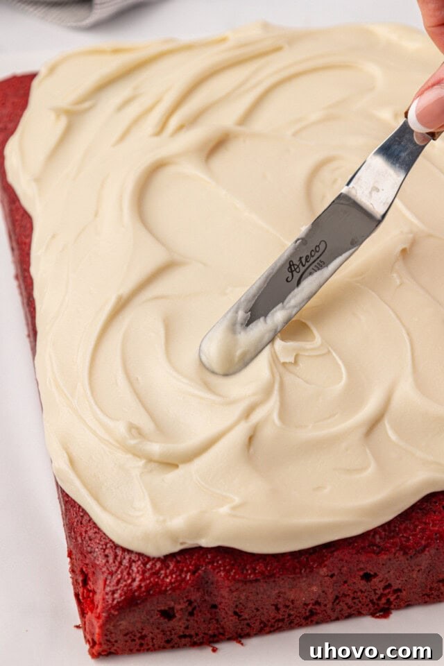 cream cheese frosting being spread over red velvet sheet cake
