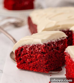 a slice of red velvet sheet cake on a cake server being removed from the remaining cake
