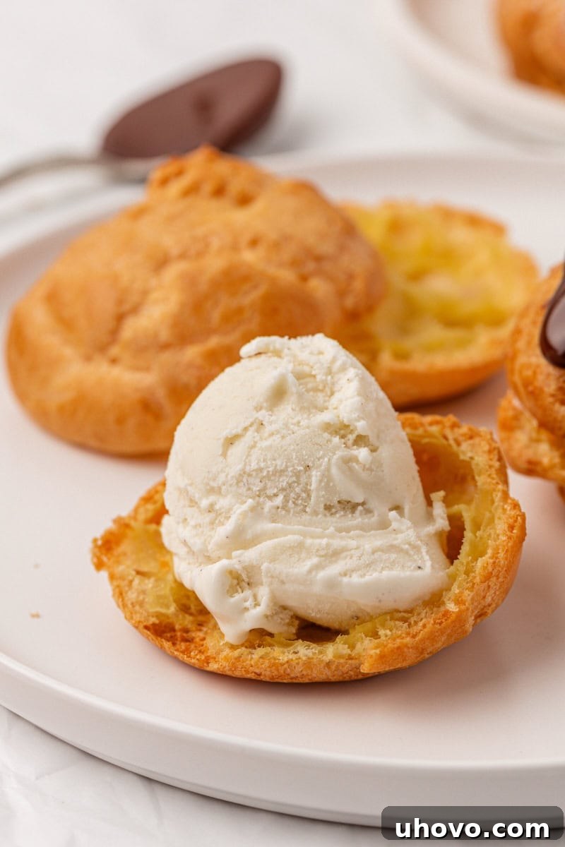 A close-up shot of a vanilla ice cream scoop carefully placed on the bottom half of a golden, hollow profiterole shell, ready for its top to be added.