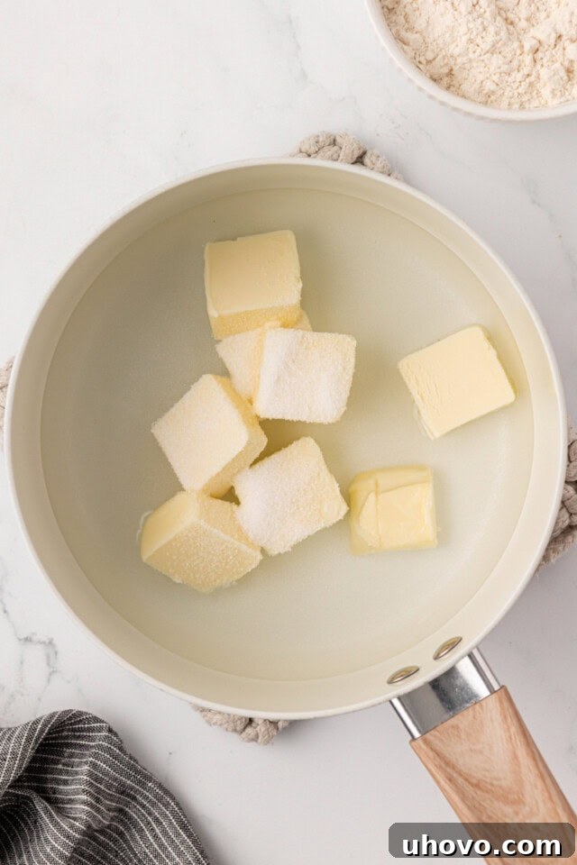 An overhead shot of a saucepan containing butter, water, a pinch of sugar, and salt, just brought to a boil on the stovetop.