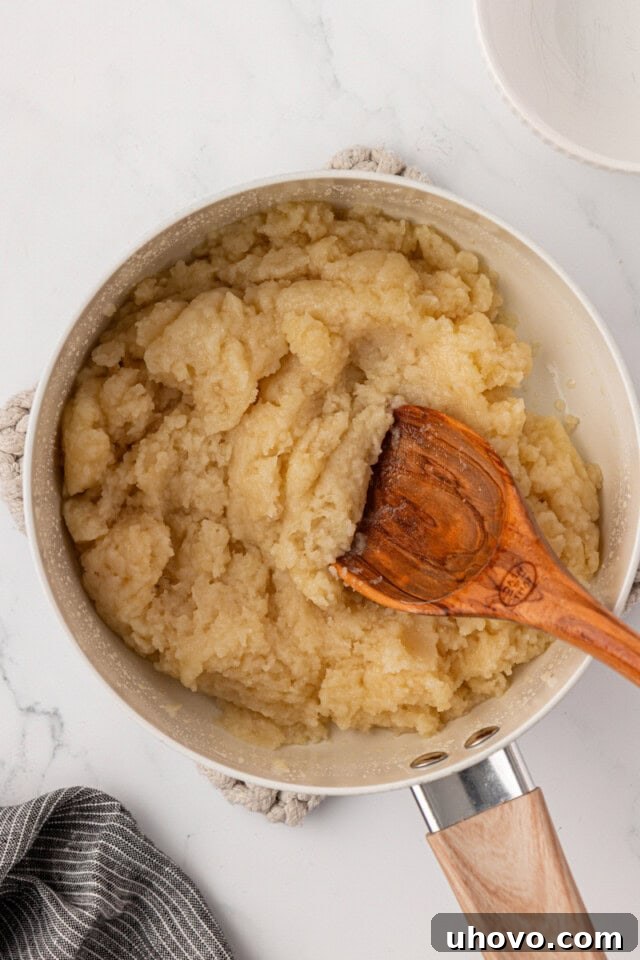 A close-up view of the pâte à choux dough in a saucepan, after flour has been vigorously stirred in, forming a smooth ball with a thin film on the pan's bottom.