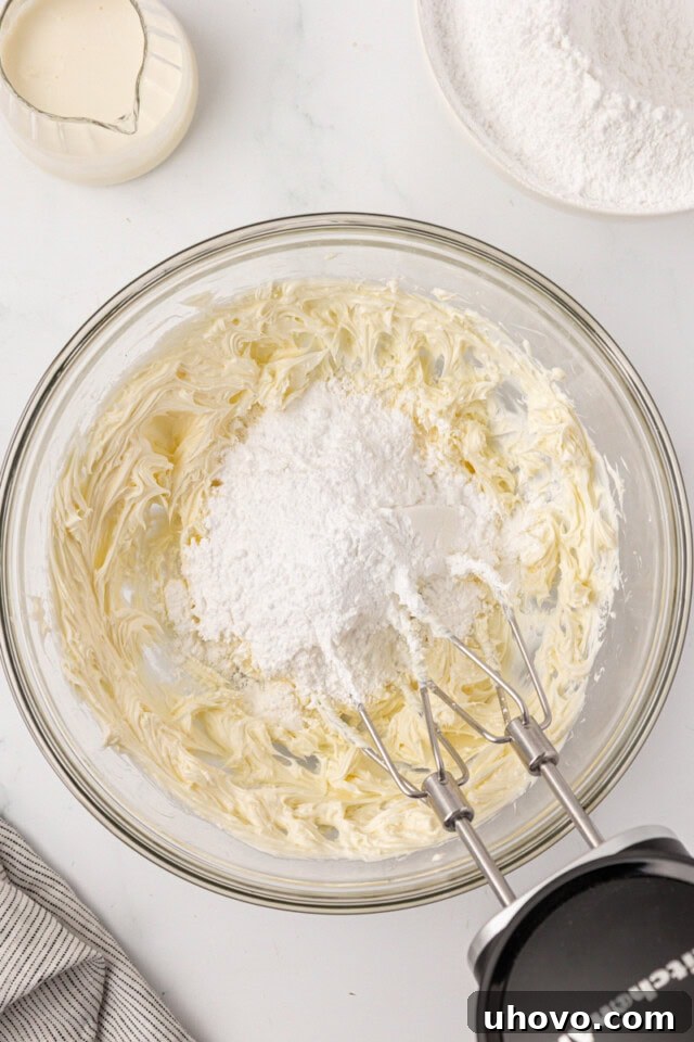 overhead view of confectioners' sugar added to creamed butter in a glass mixing bowl