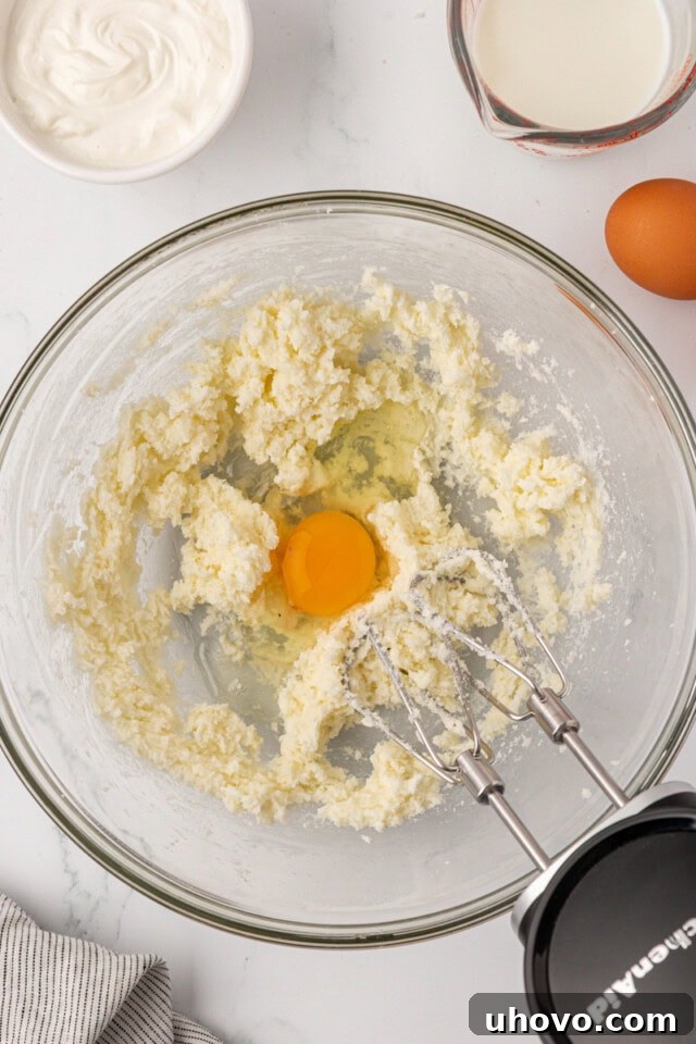 overhead view of egg added to creamed butter and sugar in a mixing bowl
