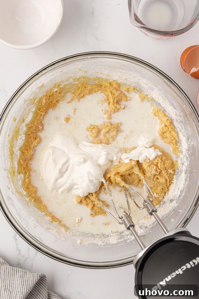 overhead view of milk and sour cream added to overhead view of dry ingredients added to wet ingredients for cookies and cream cupcake batter
