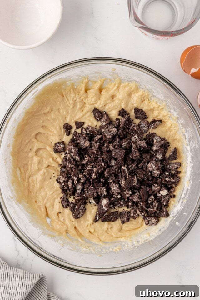 overhead view of chocolate sandwich cookie pieces added to vanilla cupcake batter