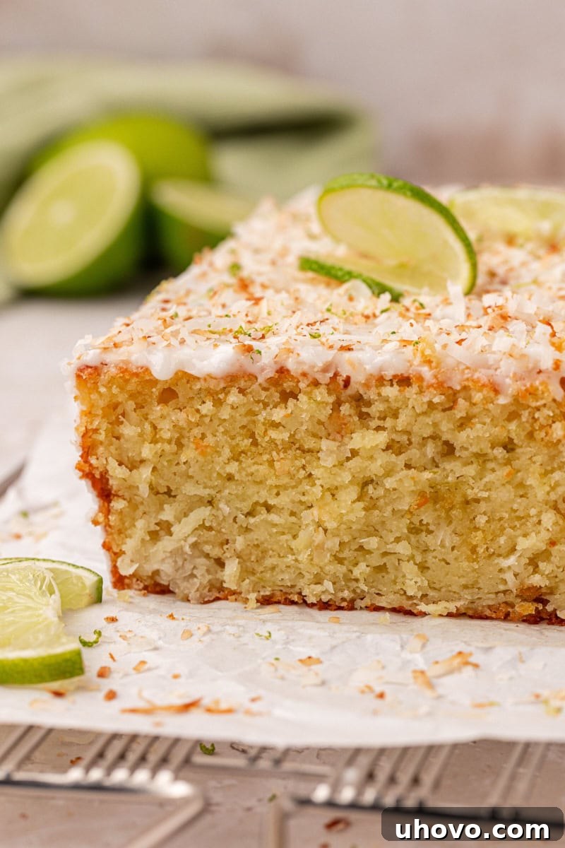 Sliced coconut lime loaf cake topped with lime glaze and toasted coconut, showing a moist, tender crumb