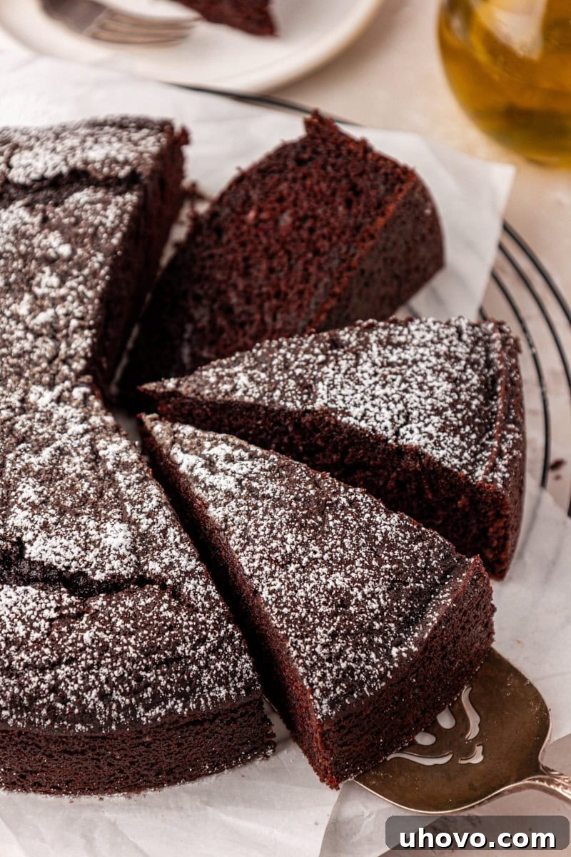 A partially sliced chocolate olive oil cake, revealing its rich, moist interior and topped with a delicate dusting of powdered sugar. The cake is soft, deeply chocolatey, and incredibly tender.