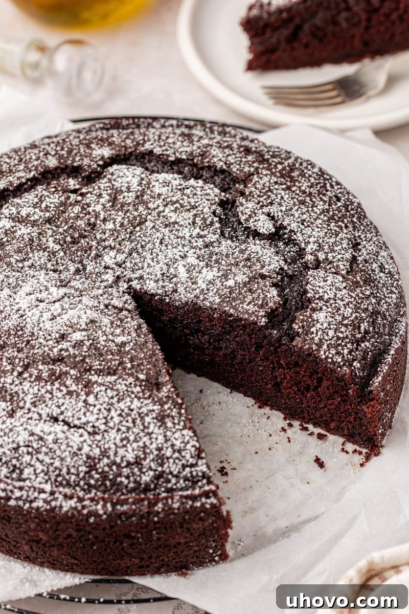 A chocolate olive oil cake, partially sliced, with one slice removed to reveal its incredibly soft and moist cake texture.