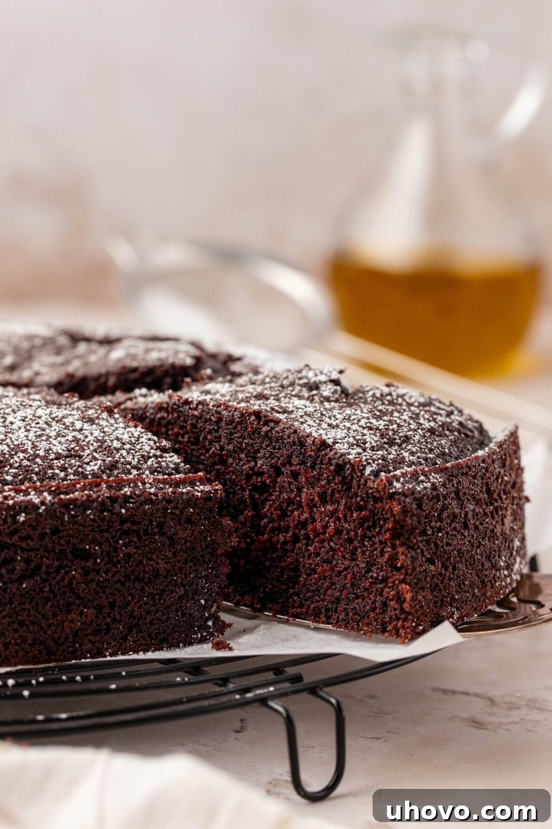 A hand gently removing a slice of rich chocolate olive oil cake from the remaining cake, highlighting its moist and enticing texture.