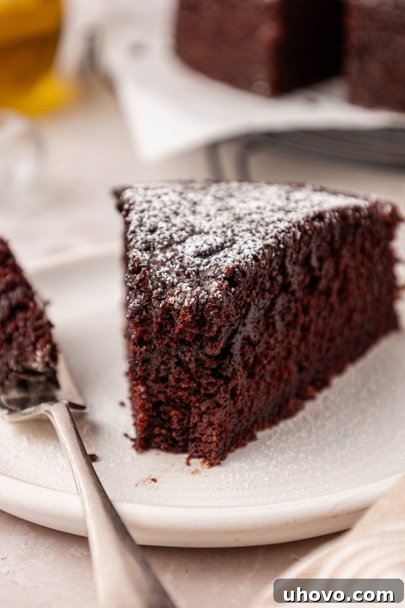 A close-up of a slice of chocolate olive oil cake on a white plate, with a bite taken out by a fork, highlighting its moist and inviting texture.