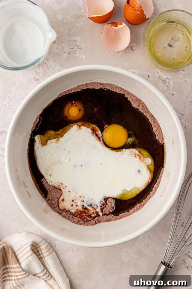 An overhead view of olive oil, eggs, vanilla extract, and buttermilk added to the dry ingredients in a mixing bowl.