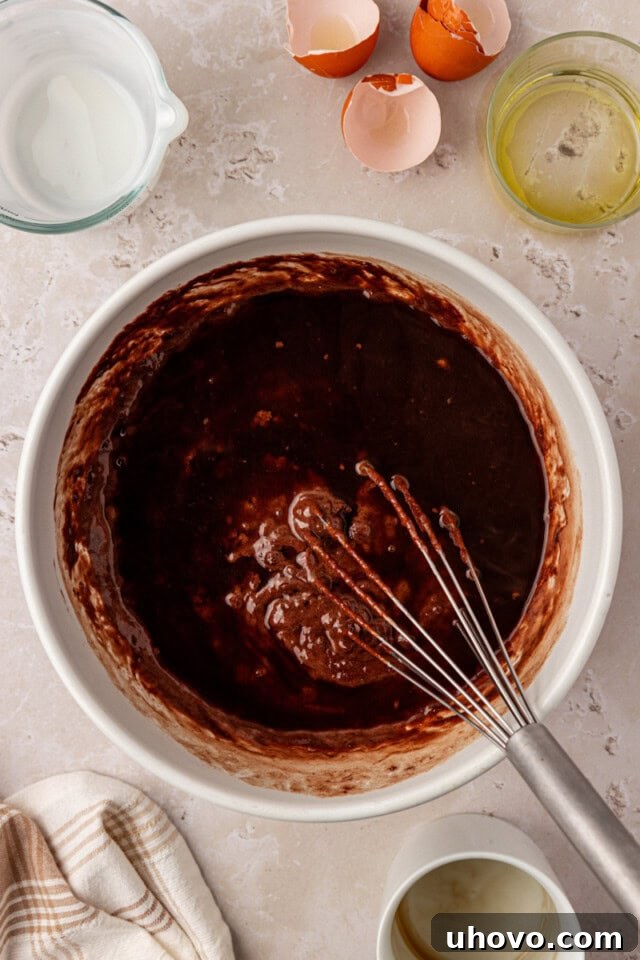 An overhead view of hot coffee being slowly poured into the chocolate olive oil cake batter in a mixing bowl, creating a smooth, glossy mixture.