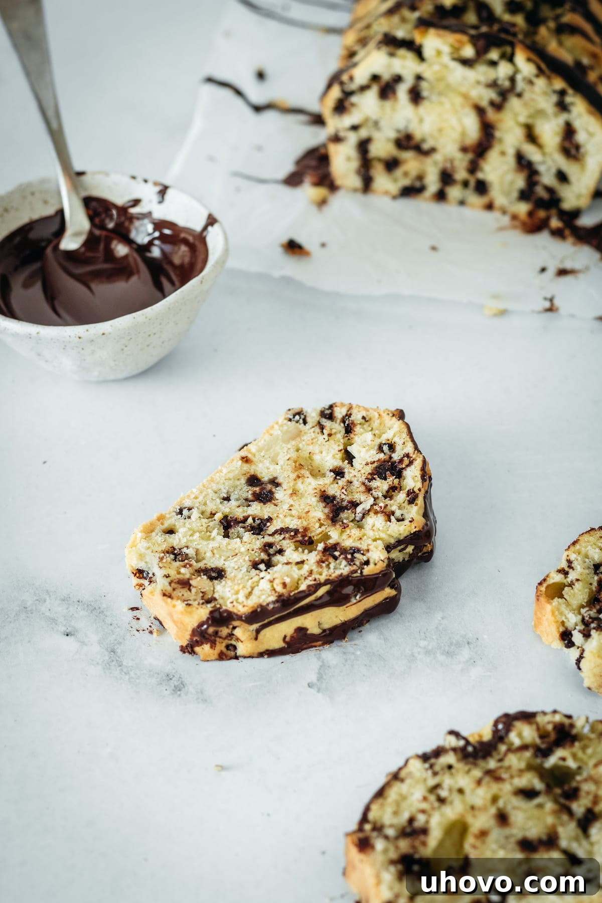 A single, inviting slice of Chocolate Chip Cashew Bread, beautifully drizzled with chocolate, resting on a sophisticated marble slab, ready to be enjoyed.