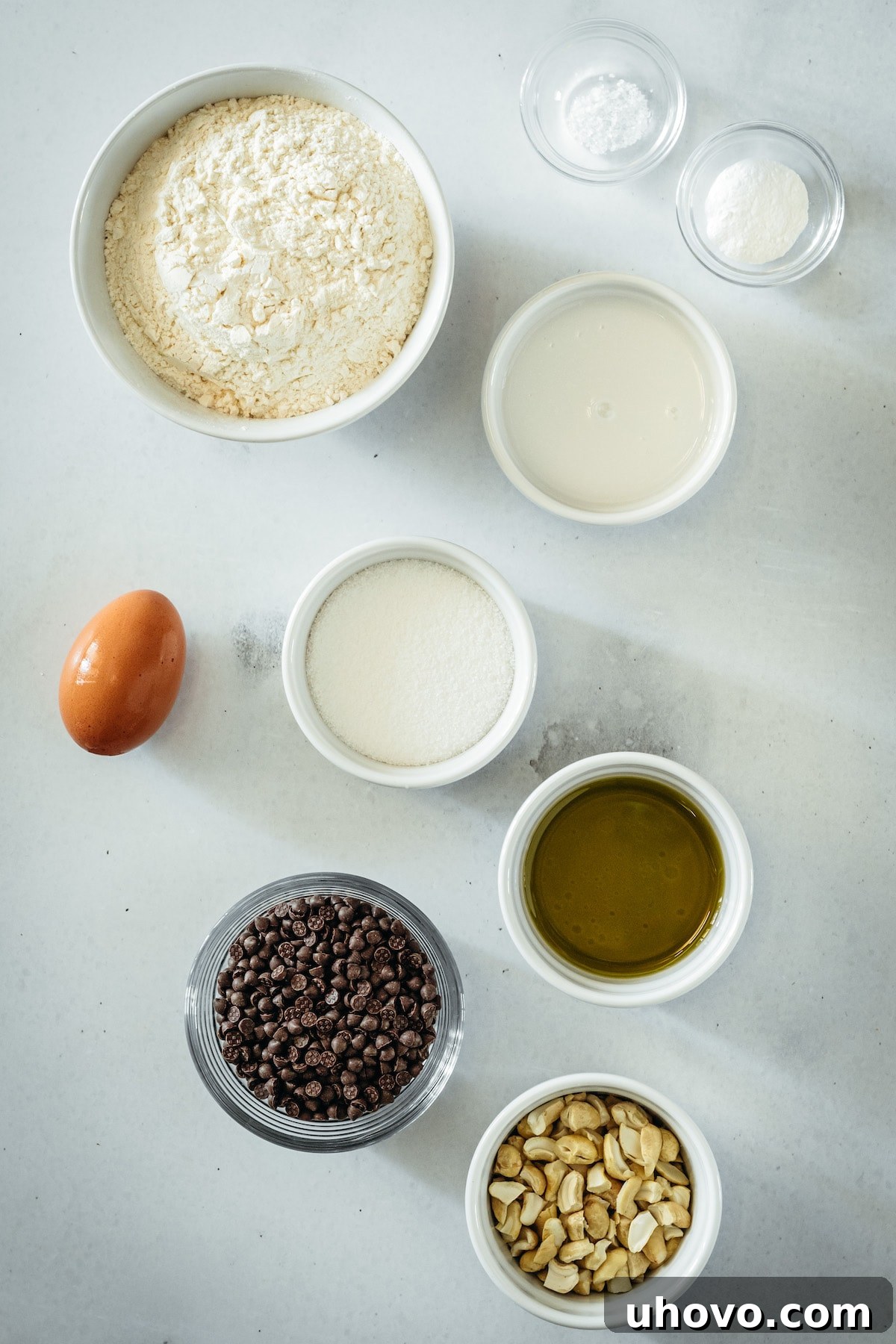 An overhead shot showcasing all the essential ingredients laid out for Chocolate Chip Cashew Bread, including flour, sugar, cashews, chocolate chips, milk, oil, and egg.
