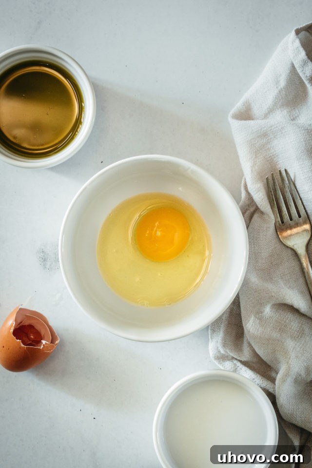 A close-up overhead shot of a single cracked large egg nestled in a small white bowl, ready to be beaten.