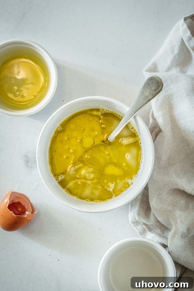 An overhead view of the wet ingredients for the bread—milk and cooking oil—mixed together in a bowl, alongside a beaten egg, ready to be combined.