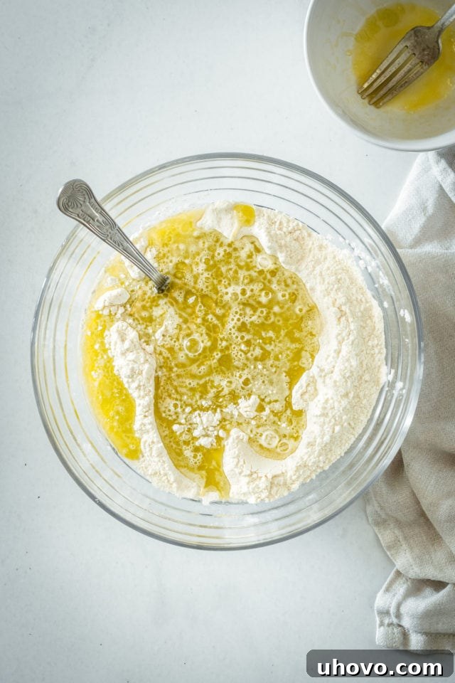 An overhead shot showing the wet ingredients being carefully poured into a well created in the center of the dry ingredients in a large mixing bowl.
