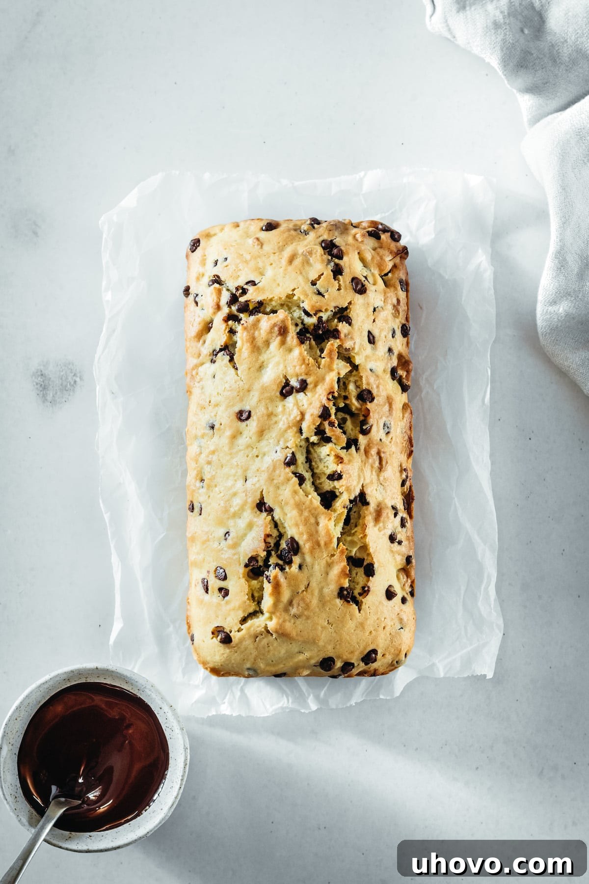 An overhead shot of the baked Chocolate Chip Cashew Bread loaf, golden brown and puffed, cooling in its pan before being drizzled with melted chocolate.