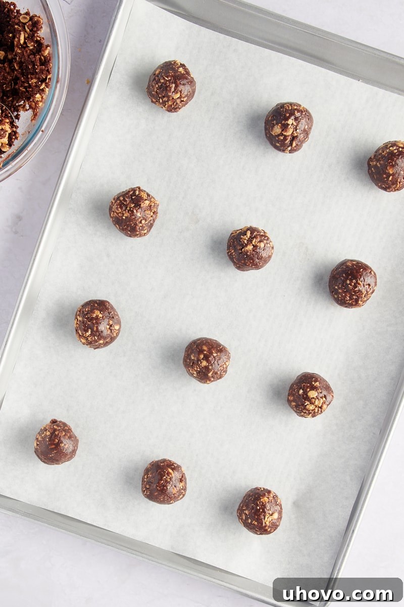 Unbaked chocolate peanut butter granola cookie dough balls on a parchment-lined baking sheet, waiting to be flattened.