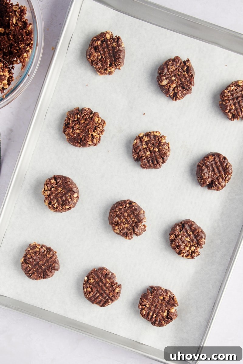 Flattened chocolate peanut butter granola cookie dough rounds arranged on a parchment-lined baking sheet, ready for the oven.