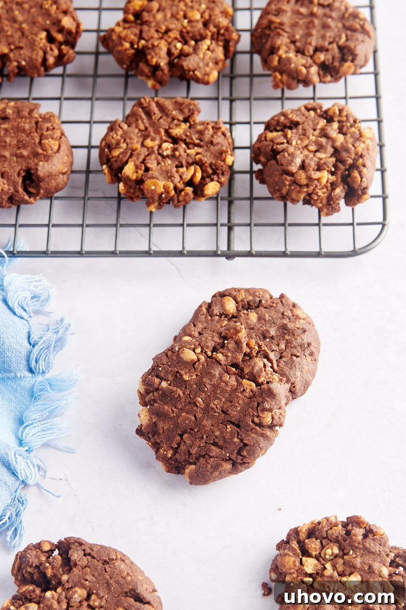 Freshly baked chocolate peanut butter granola cookies cooling on a wire rack, with some artfully arranged on a wooden tabletop.