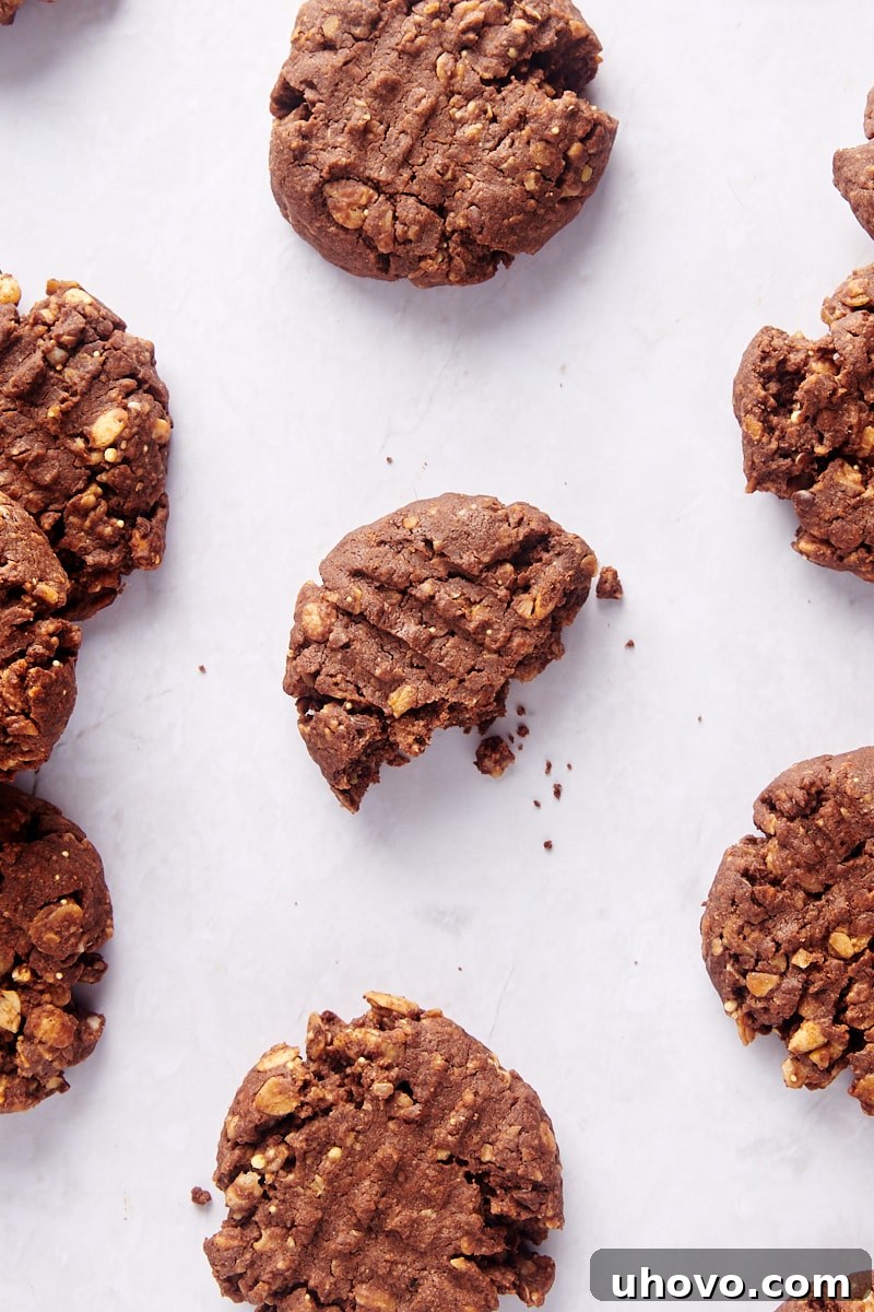Close-up overhead view of chocolate peanut butter granola cookies on parchment paper, with a bite taken out of one in the center, revealing its chewy interior.