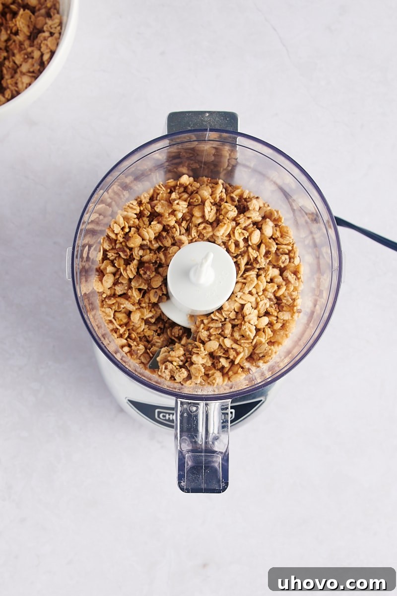 Granola in a food processor bowl before being ground into a fine texture.