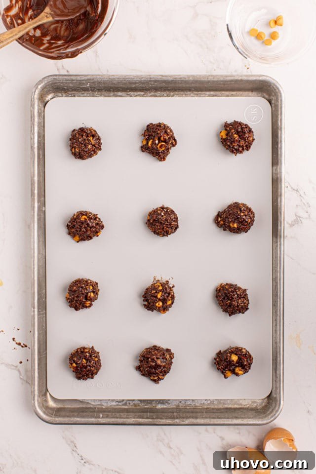 Overhead view of scooped portions of chocolate butterscotch cookie dough evenly spaced on a parchment-lined baking sheet.