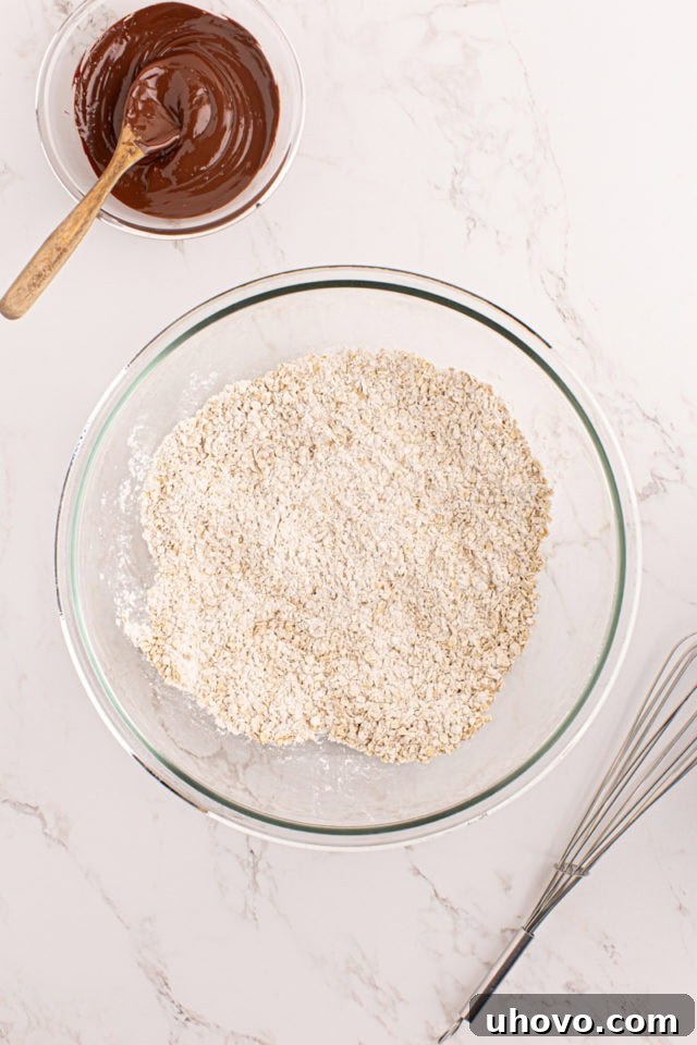 Overhead view of dry ingredients for chocolate butterscotch cookies (flour, baking soda, salt, oats) in a mixing bowl, ready to be whisked.