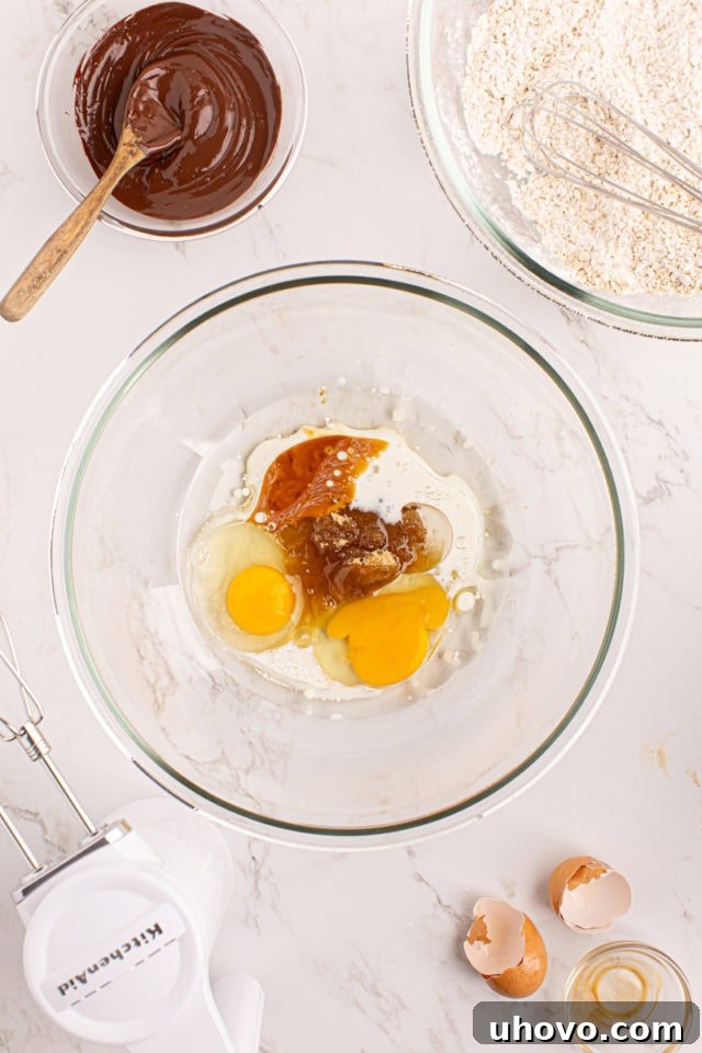 Overhead view of wet ingredients (oil, brown sugar, eggs, milk, vanilla) in a mixing bowl before combining, ready for beating.